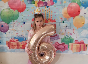 Dziewczynka trzyma balon w kształcie cyfry 6.