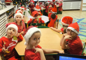 Grupa jagód w odświętnych czerwonych strojach siedząca przy stolikach w sali