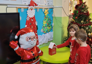 Dwoje dzieci wrzuca list do skrzynki pocztowej Świętego Mikołaja