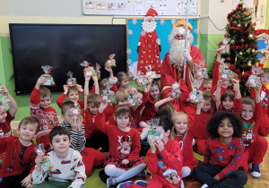 Dzieci w grupie Zajączki podnoszą do góry upominki jakie dostały od Mikołaja