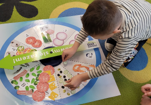 Chłopiec układa składniki na pizzy logopedycznej na dana głoskę