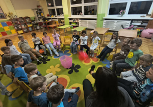 Dzieci biorące udział w zabawie "Balon do kosza", ich zadaniem jest tak podawać balon, aby trafił do ustawionego w środku kosza, bez użycia rąk