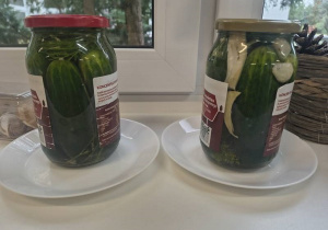 Dwa słoiki pełne ogórków stoją na parapecie w klasie i zachodzi w nich proces kiszenia.