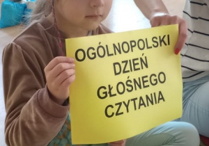 Dziewczynka trzyma kartkę z napisem Ogólnopolski Dzień Głośnego Czytania
