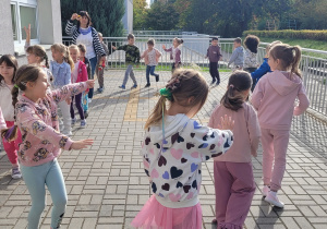 Dzieci idą po obwodzie koła wykonując naprzemienne wymachy rąk.