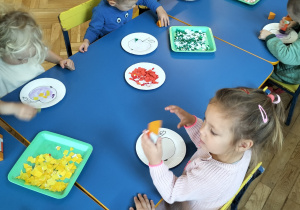 dzieci siedzą przy stolikach- wykonują pracę plastyczną - wydzieranie z papieru kolorowego i wyklejają sylwetę jabłka